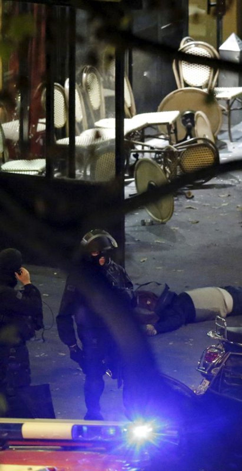 French special forces policemen stand next to a victim on the sidewalk outside a cafe at the Bataclan concert hall following fatal shootings in Paris