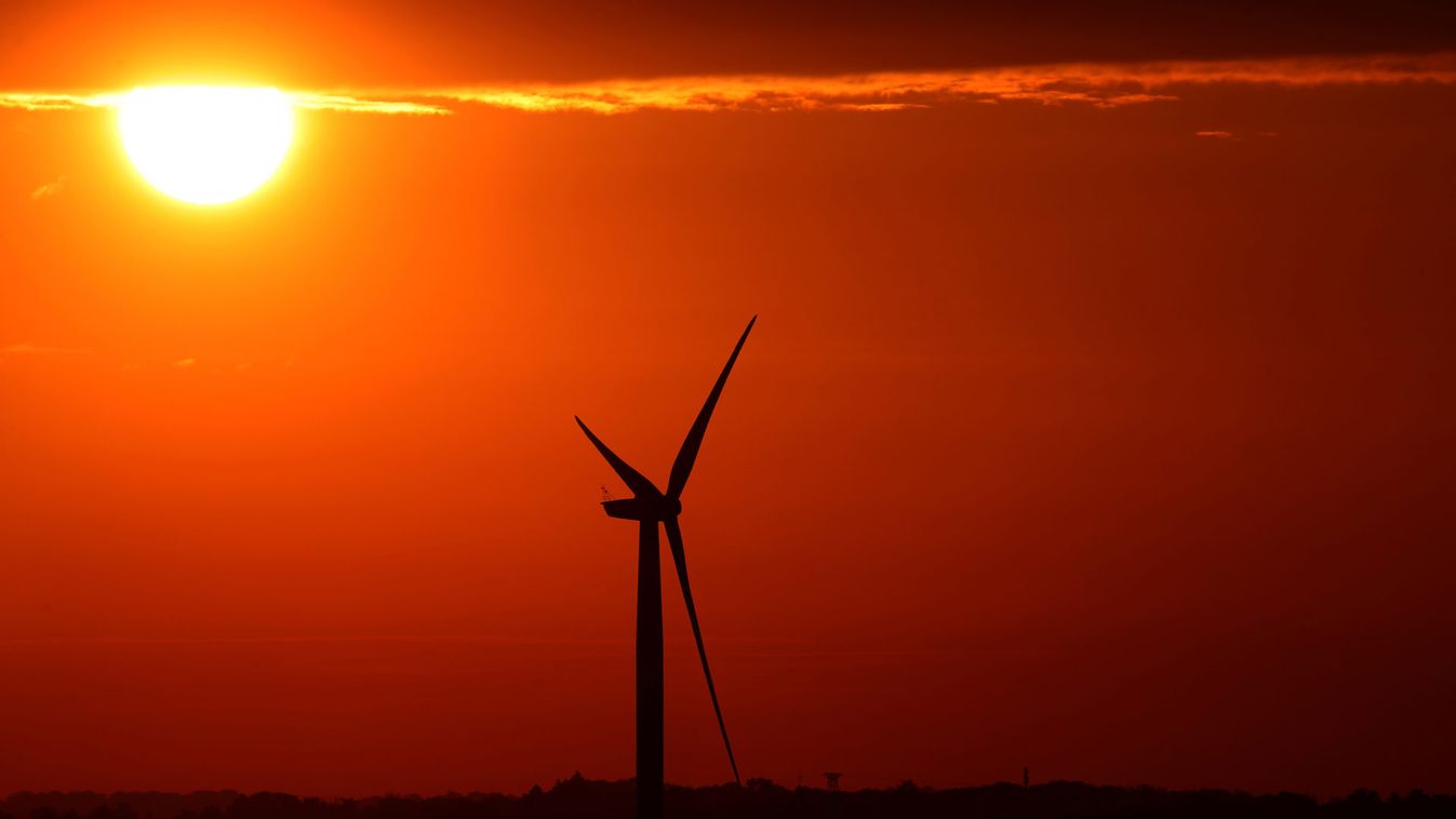 The sun rises behind a wind mill in Halle