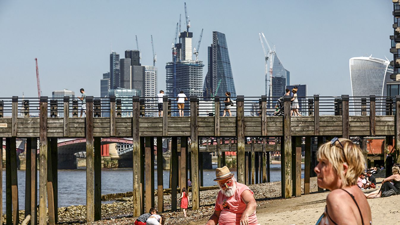 A man sunbathes on the banks of the River Thames in view of London financial district in London