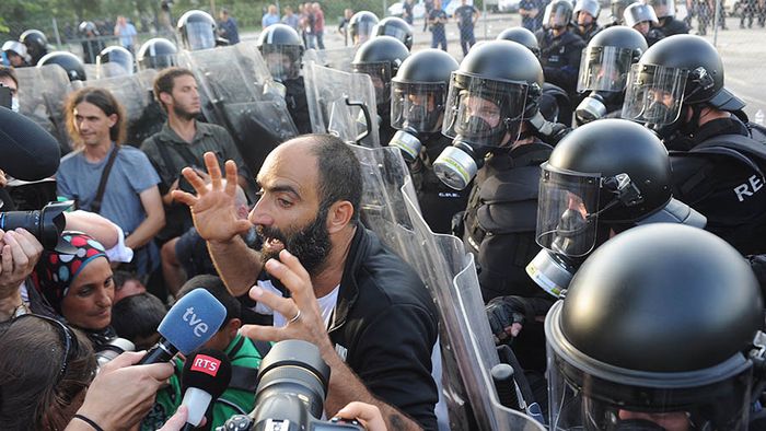 A migrant talks to the media in front of Hungarian riot police at the border crossing with Serbia in Roszke