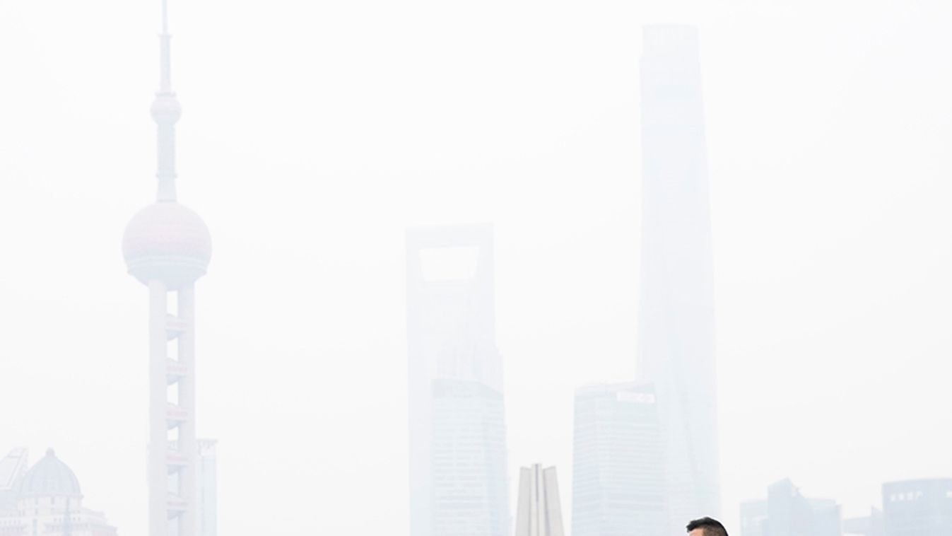 A man wearing a face mask rides a bicycle on a bridge in front of the financial district of Pudong covered in smog during a polluted day in Shanghai