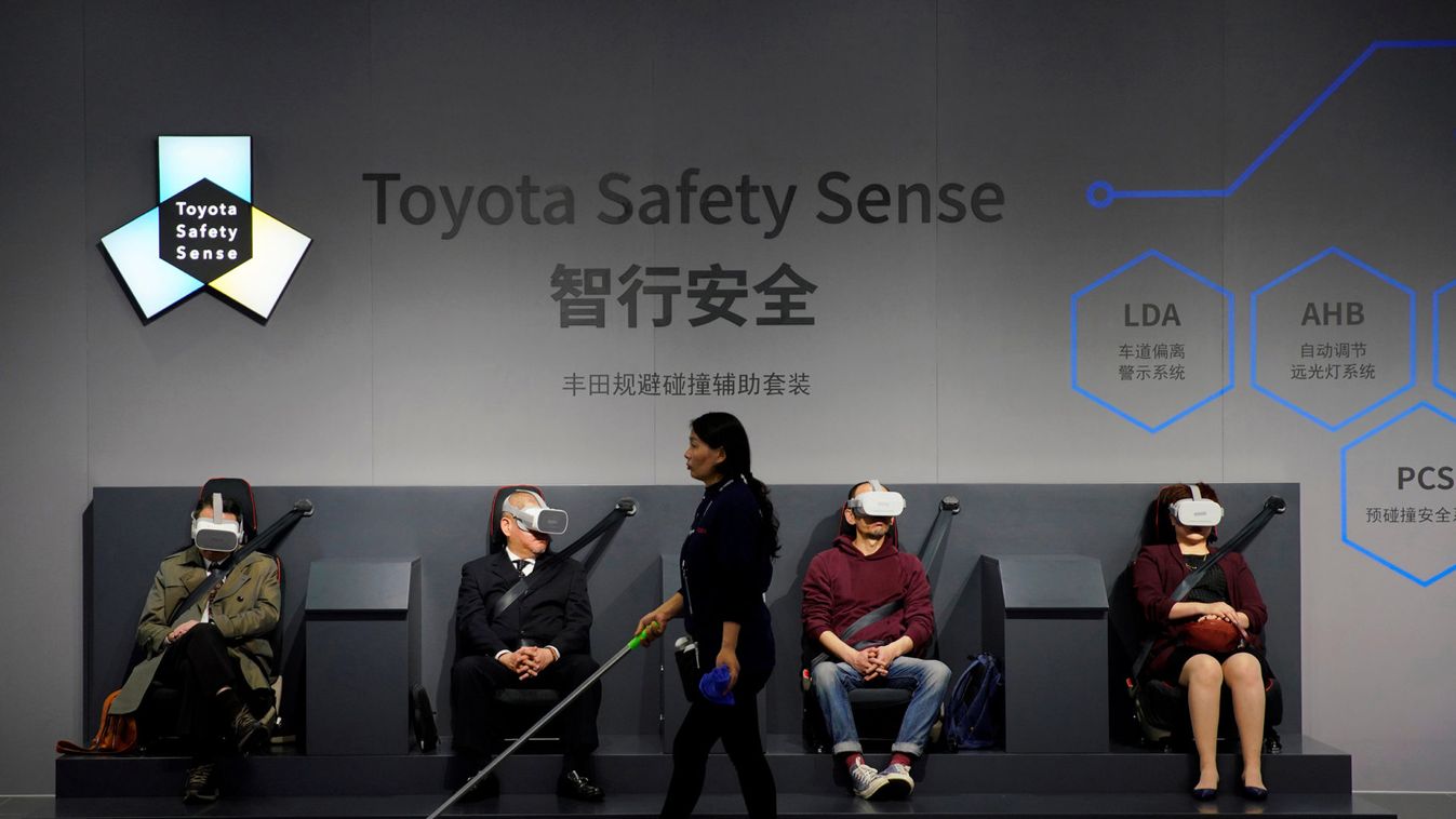 Cleaner walks past visitors wearing VR goggles at a booth for Toyota Safety Sense during the media day for the Shanghai auto show in Shanghai