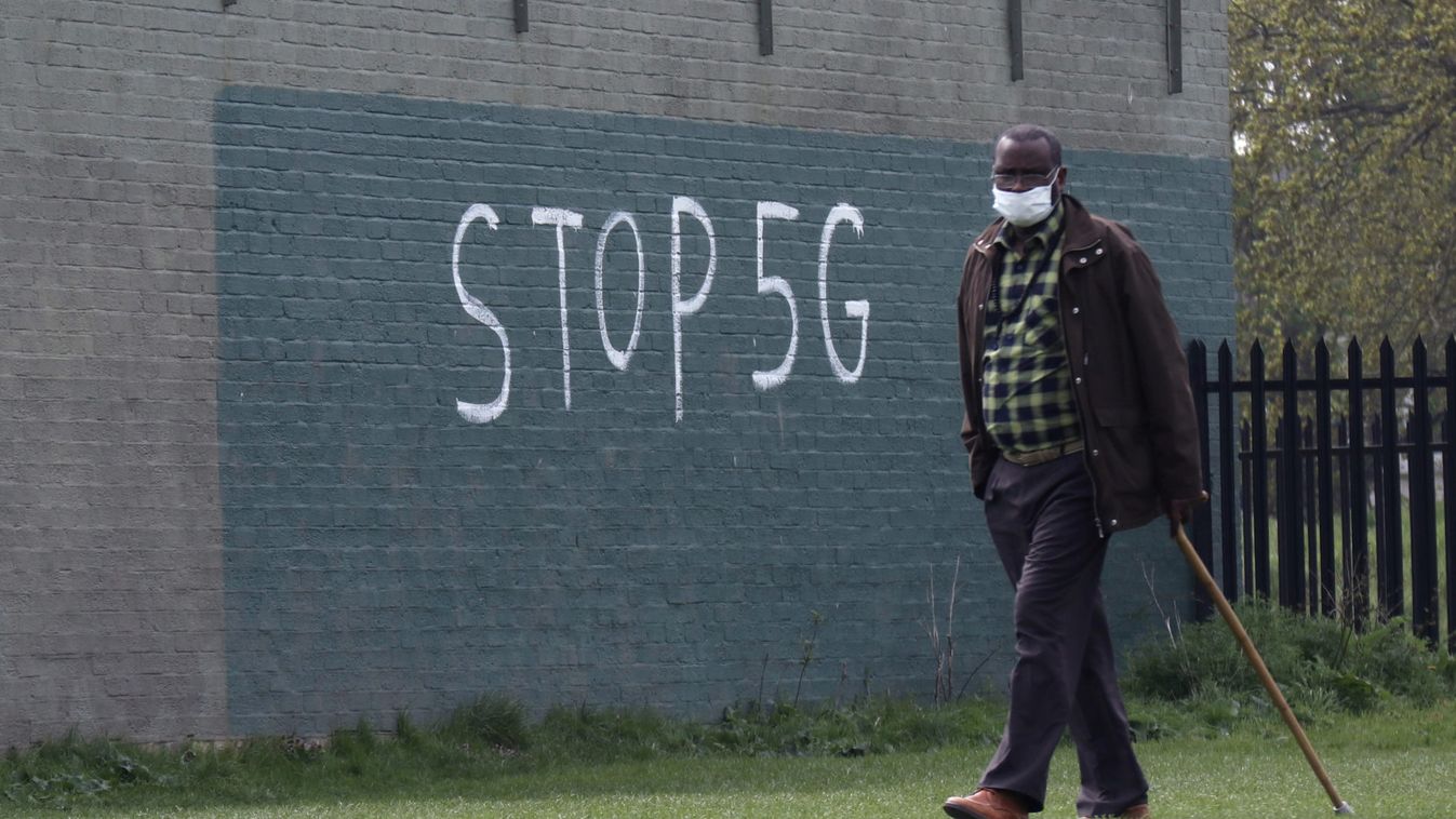 A man wearing a face mask during an outbreak of coronavirus disease (COVID-19) walks past a graffiti that reads "STOP 5G" in London