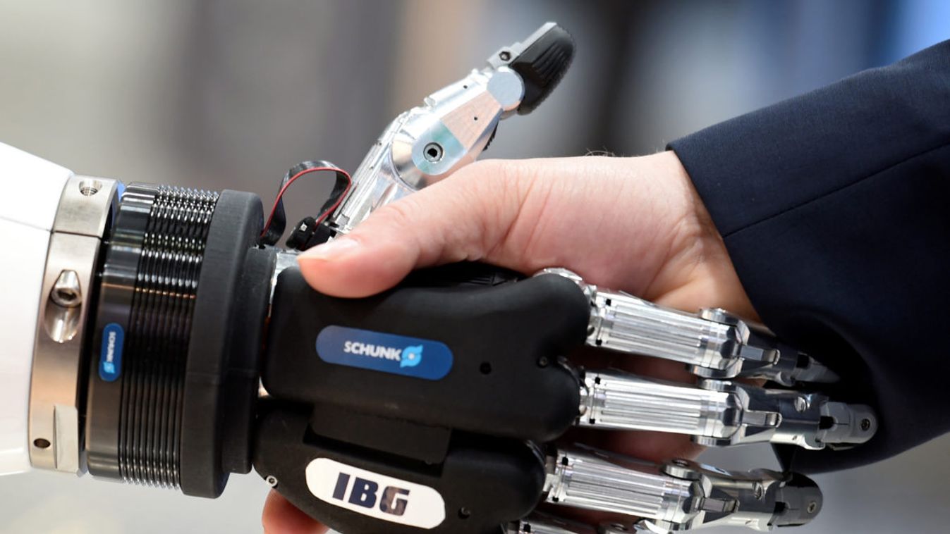 A visitor shakes hands with a humanoid robot at the booth of IBG at Hannover Messe, the trade fair in Hanover