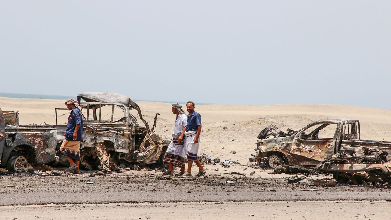 People walk past the wreckage of government forces vehicles destroyed by UAE air strikes near Aden