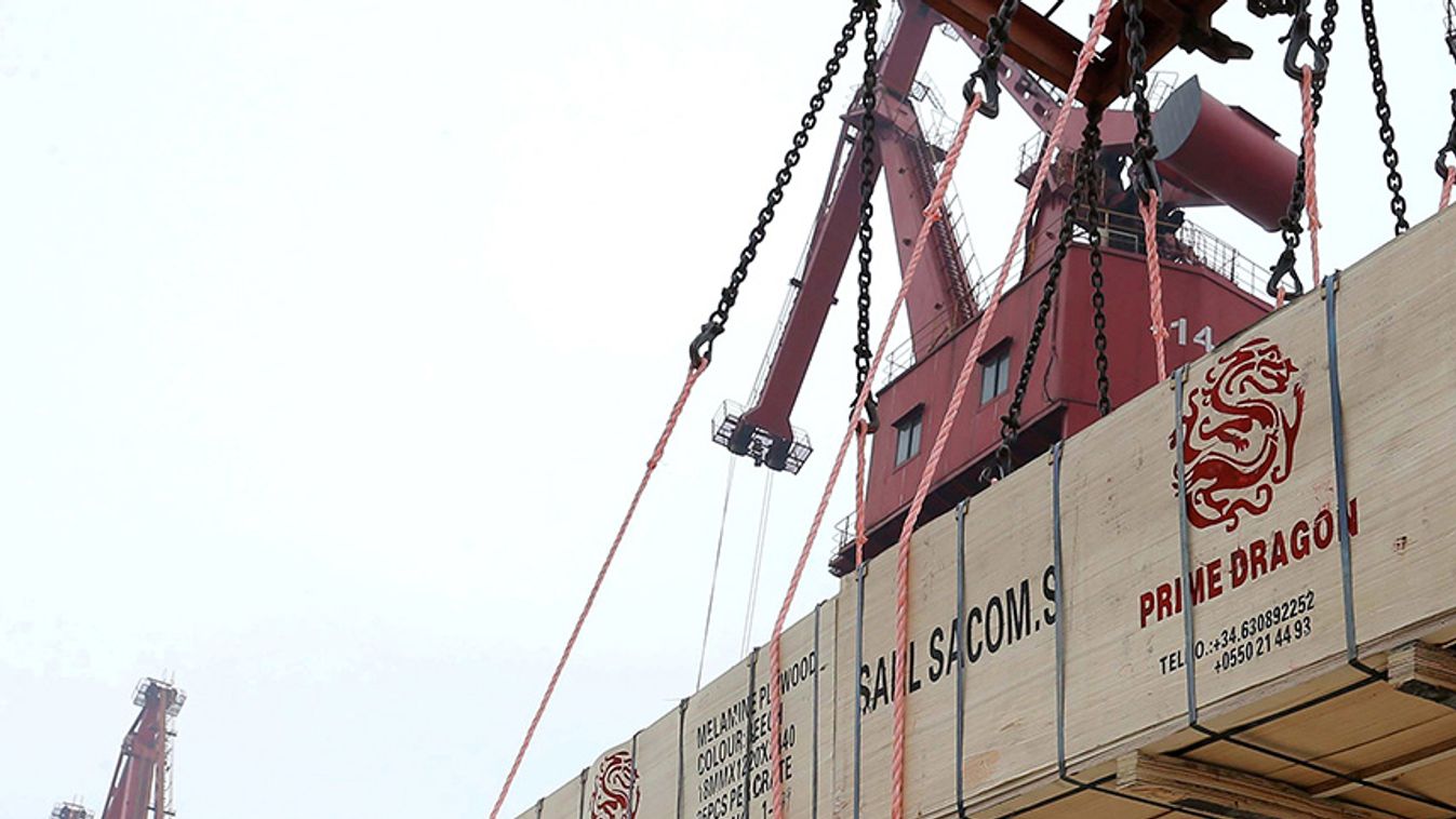 Worker gestures as a crane lifts goods for export onto a cargo vessel at a port in Lianyungang, Jiangsu