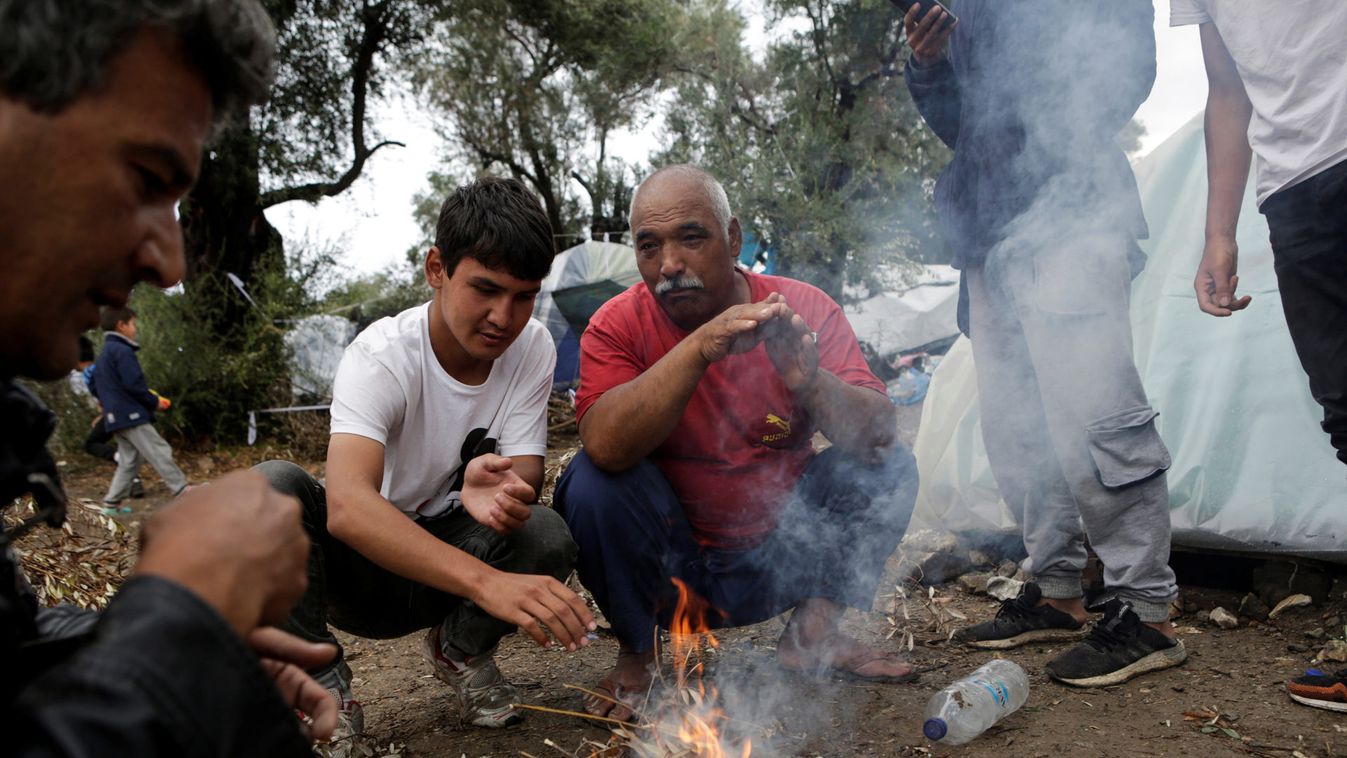 Men warm themselves next to a fire at a makeshift camp for refugees and migrants next to the Moria camp, following a rainfall on the island of Lesbos