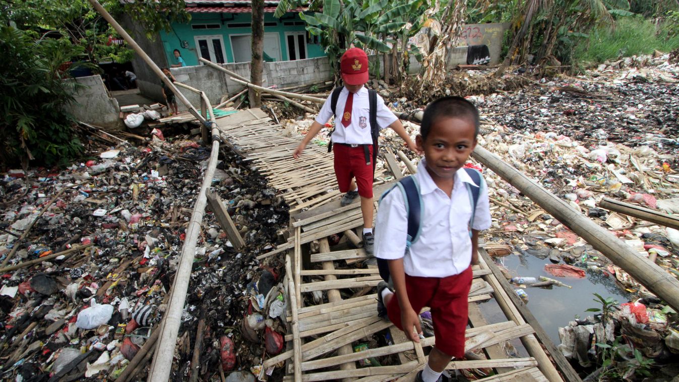 Students cross a bamboo bridge above a garbage-filled stream branching off the Ciliwung River in Bogor