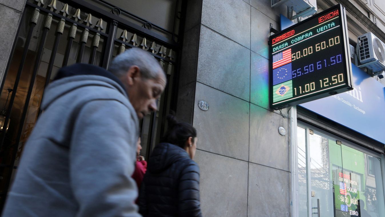 Pedestrians walk past an electronic board showing currency exchange rates in Buenos Aires' financial district
