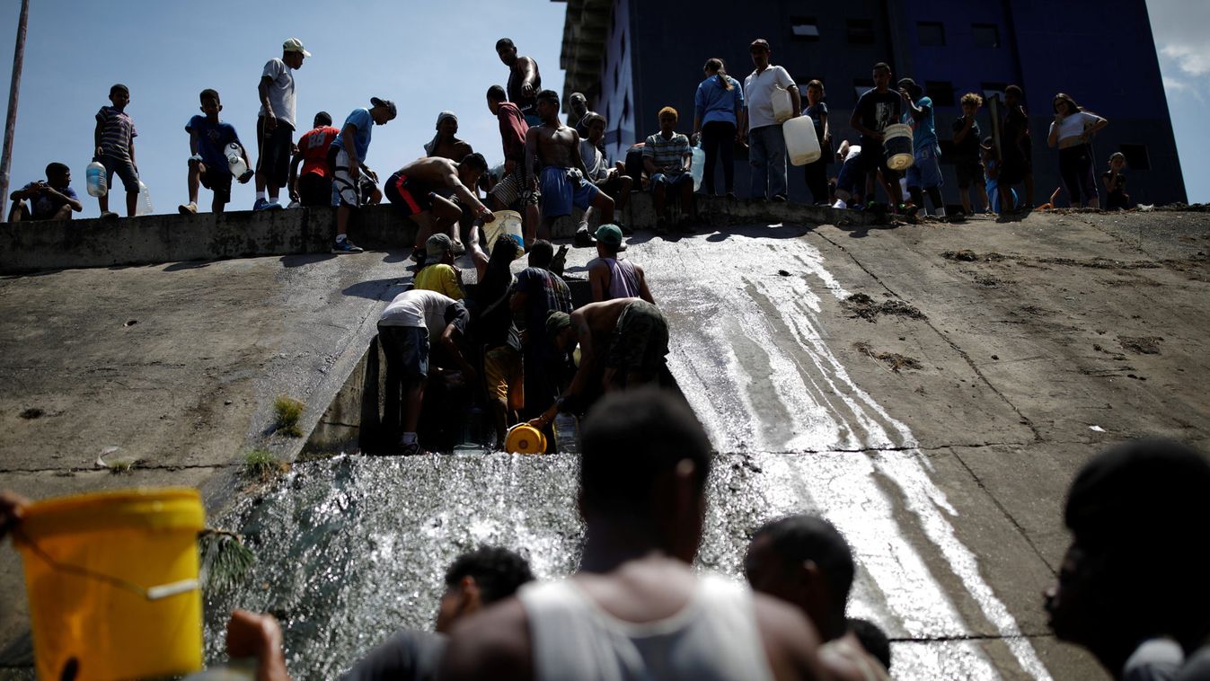 People collect water released through sewage drain that feeds into the Guaire River in Caracas