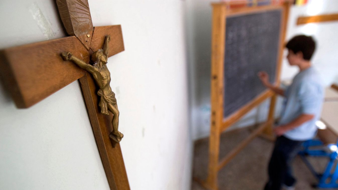 A crucifix is seen on a wall as a student writes on a blackboard in a school classroom in Rome