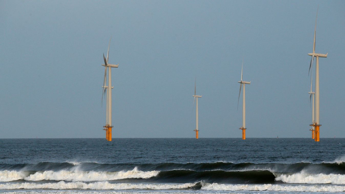 A couple walk their dog on Redcar beach past an offshore wind farm in Redcar
