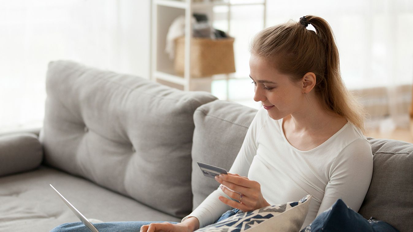 Young woman sitting on couch using laptop and credit card