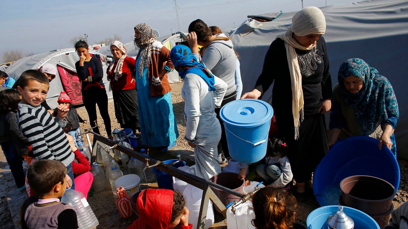 Kurdish refugees from the Syrian town of Kobani wait to fill their jerrycans around a clean water source at a refugee camp in the border town of Suruc