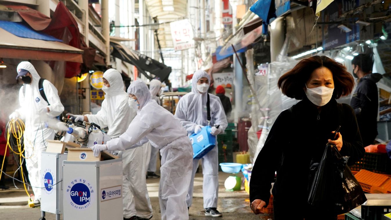A woman wearing a mask to prevent contracting the coronavirus reacts as employees from a disinfection service company sanitize a traditional market in Seoul