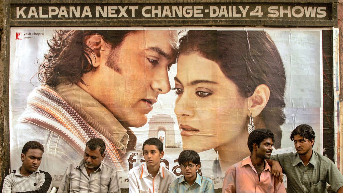 Men sit in front of poster of "Fanaa" outside movie theatre in Mumbai
