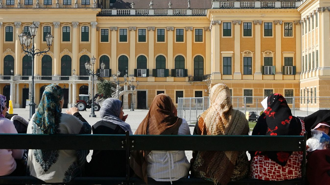 Women and children enjoy the morning sun on a bench in front of Schoenbrunn castle in Vienna