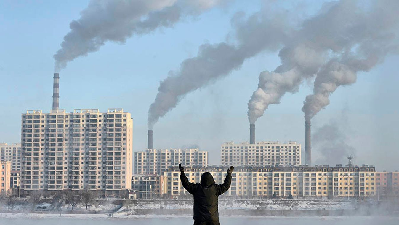An elderly man exercises in the morning as he faces chimneys emitting smoke behind buildings across the Songhua river in Jilin