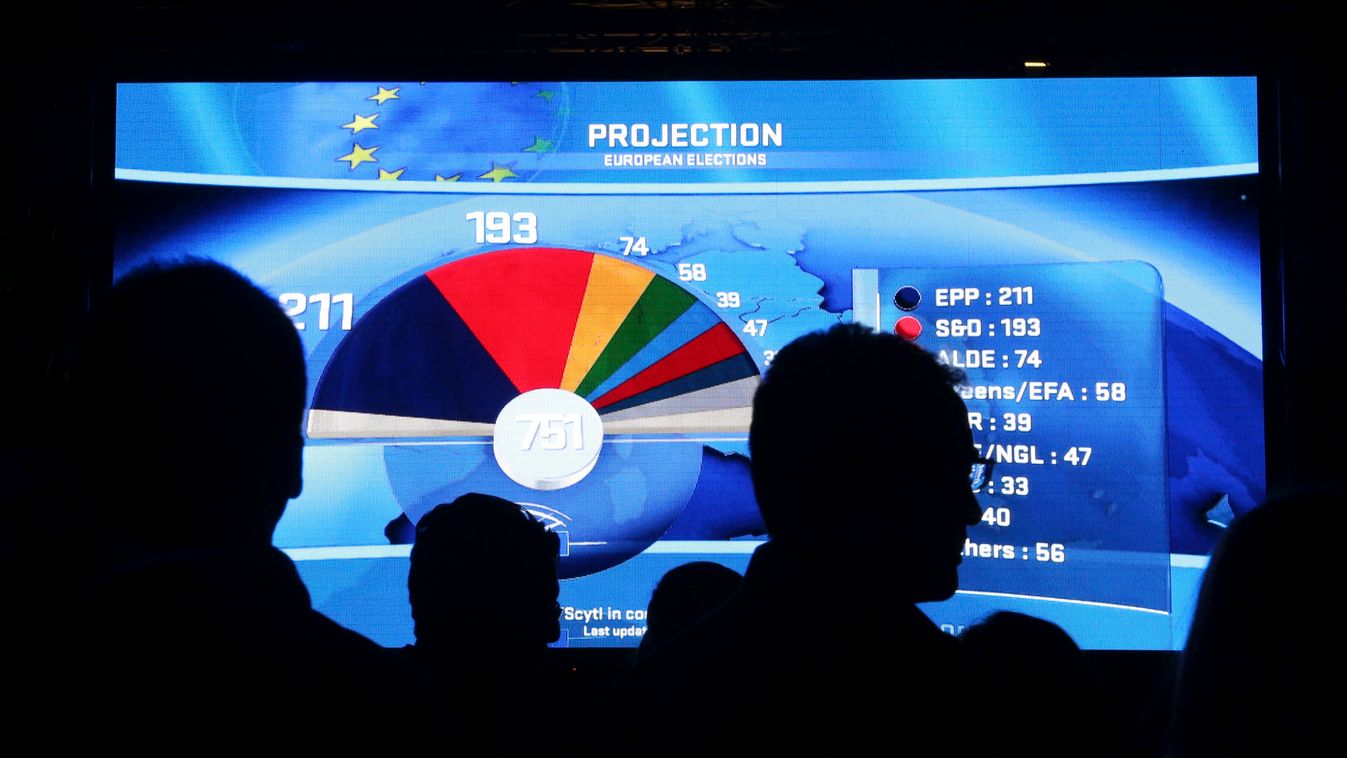 People watch a board displaying provisional results of the European Parliament election at the EU Parliament in Brussels