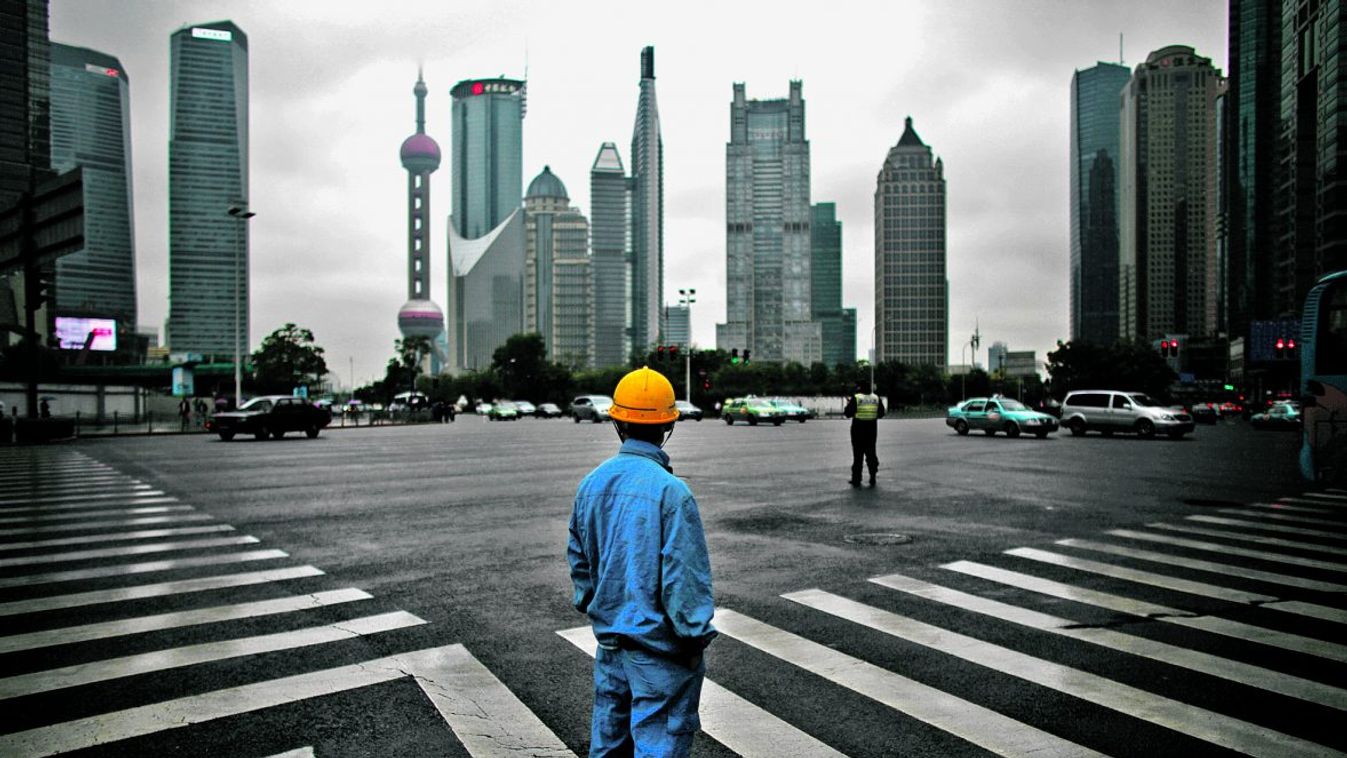 Sanghaj felhőkarcolóit nézi egy átkelésre váró munkás