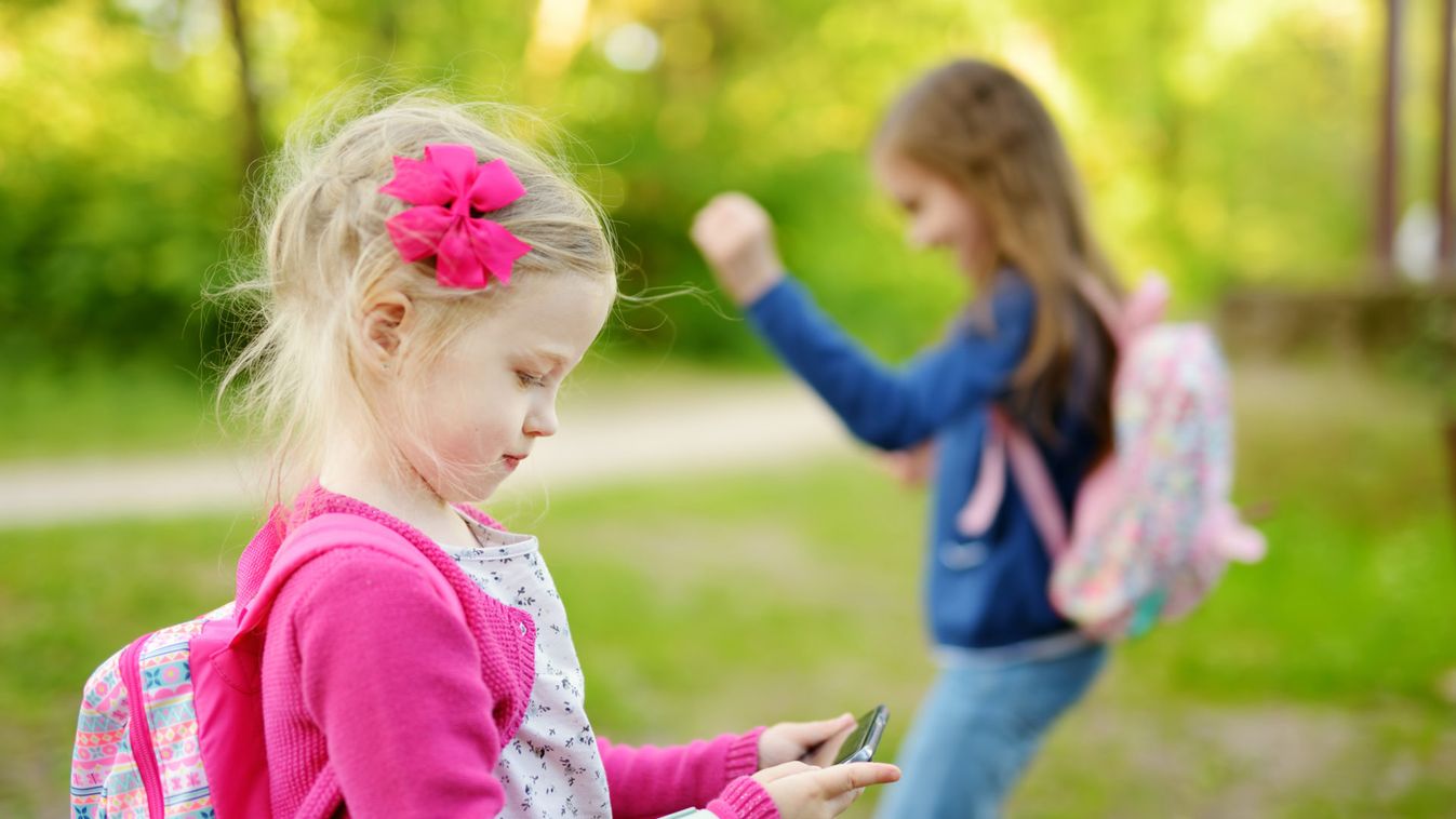 Two cute little sisters playing outdoor mobile game on their smart phones.