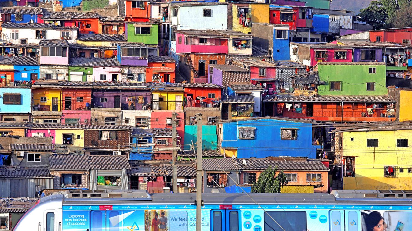 A metro train moves past a cluster of houses at the Asalpha slum in Mumbai