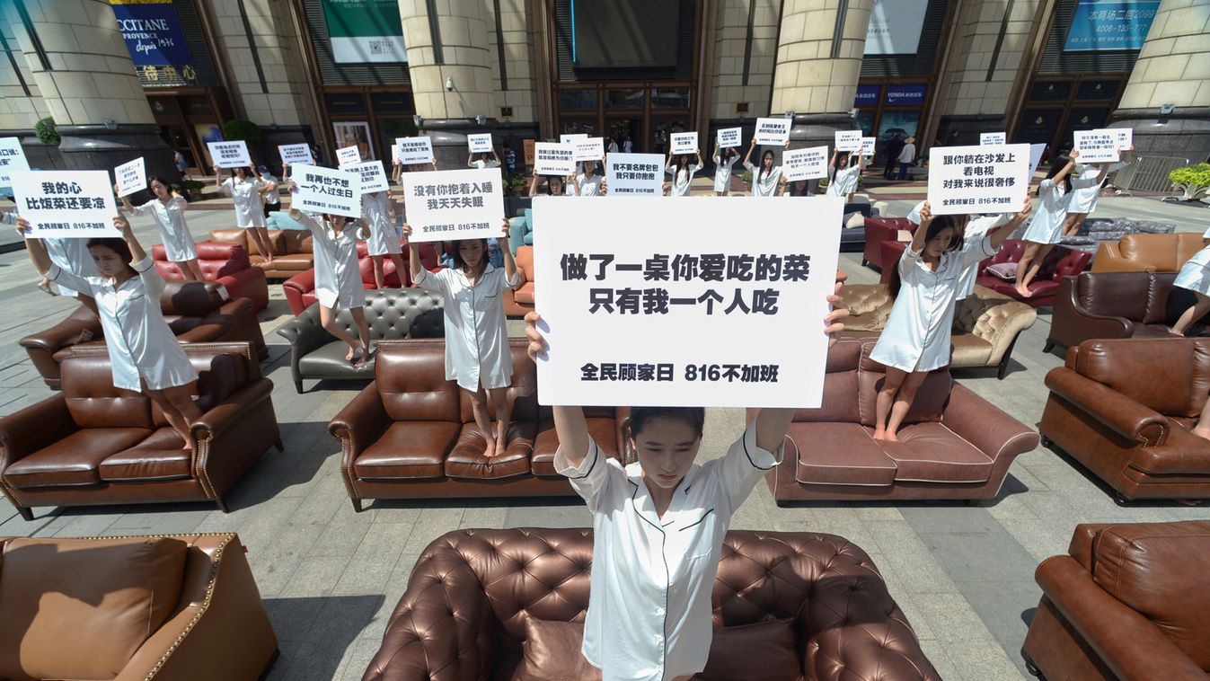 Participants hold placards as they stand on sofa during a performance art to protest against husbands who overworked, in Shanghai