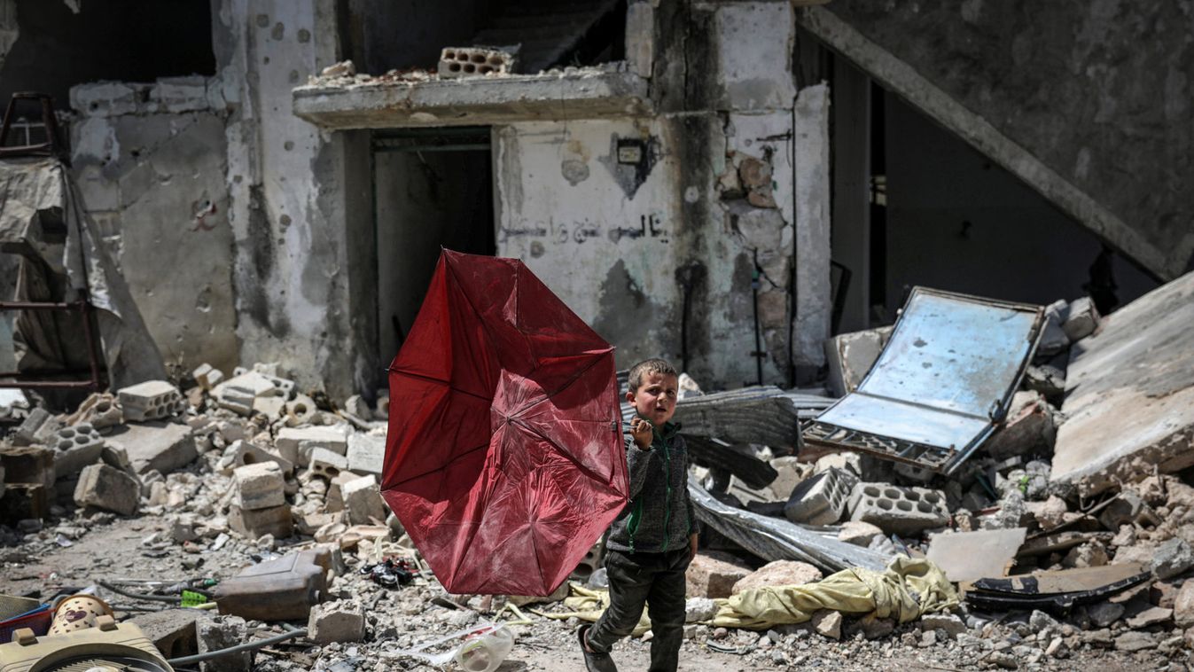 A boy carries a broken umbrella as he walks past a damaged building in the rebel-held town of Nairab