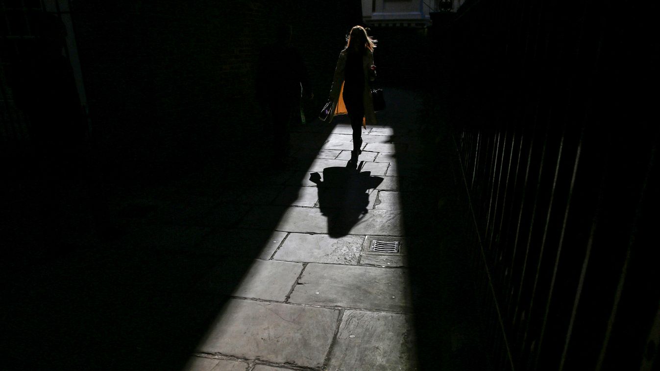 A woman casts a shadow as she walks along an alleyway in central London