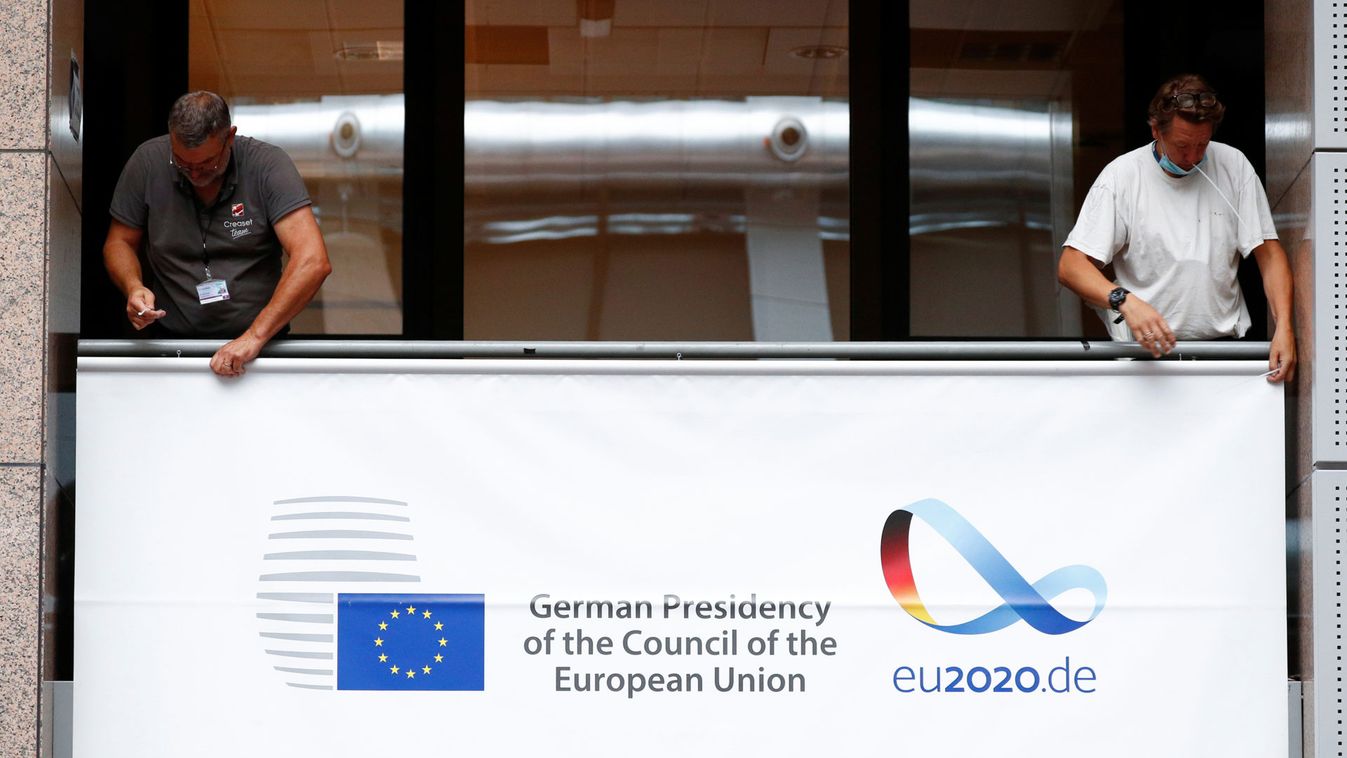 Workers install a banner at the EU Council marking the taking over of the rotating presidency of the European Council by Germany, in Brussels
