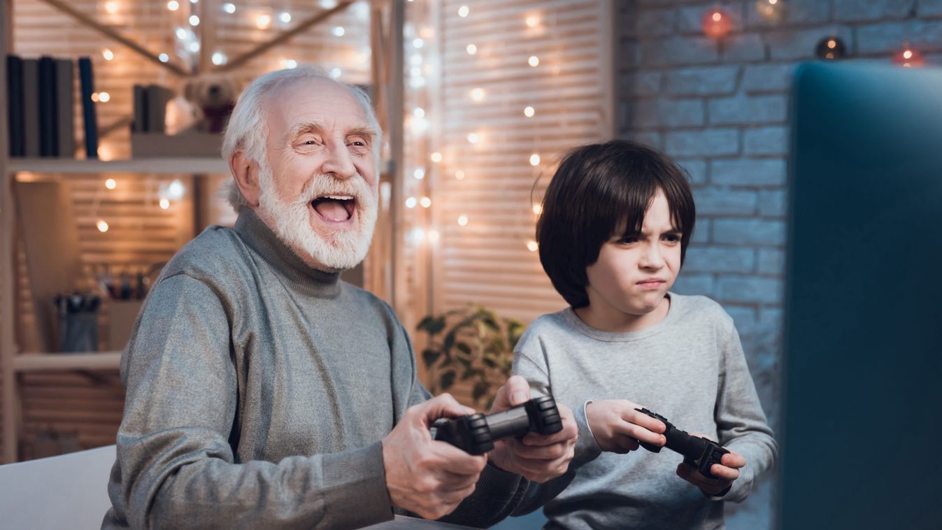 Grandfather and grandson are playing video games on computer at night at home.