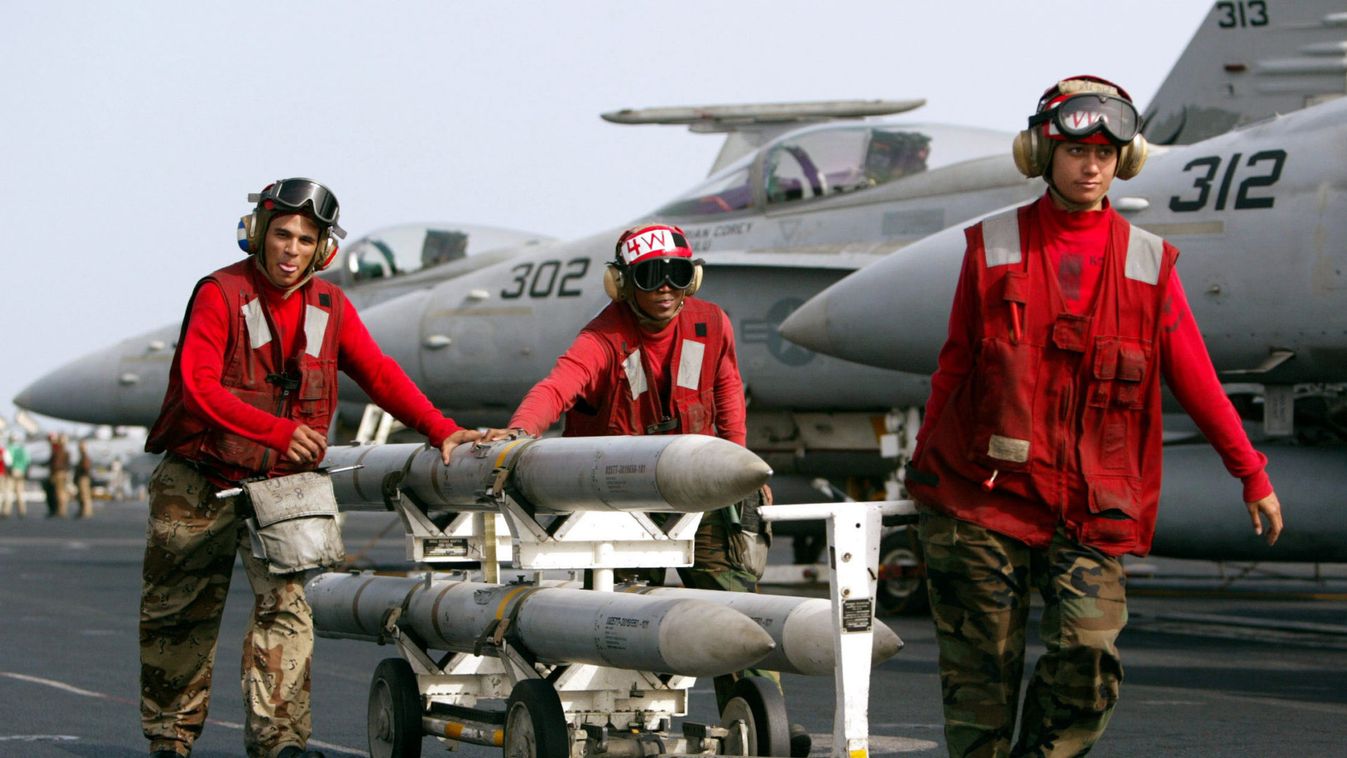 AIM-120 AMRAAM air-to-air intercept missiles are wheeled past fighter jets on the deck of the USS Ki..
