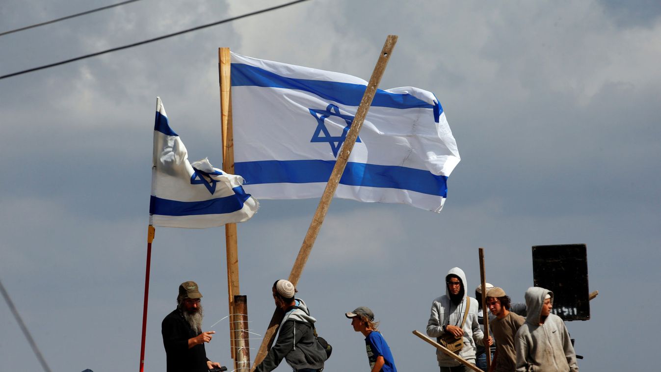 Protestors carry wooden sticks as they stand on a roof during the evacuation of Jewish settler families from the illegal outpost of Netiv Ha'avot in the occupied West Bank