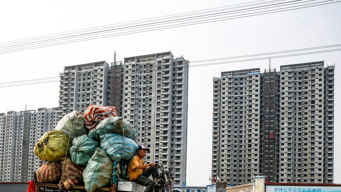 People drive tricycles carrying bags with recycling material past a construction site of residential highrises in Beijing
