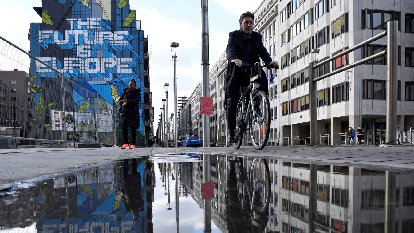 People are reflected in a puddle as they pass by a mural near the EU headquarters in Brussels