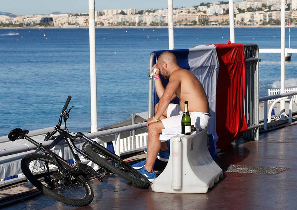 A man reacts as he sits near a French flag along the beachfront the day after a truck ran into a crowd at high speed killing scores celebrating the Bastille Day July 14 national holiday on the Promenade des Anglais in Nice