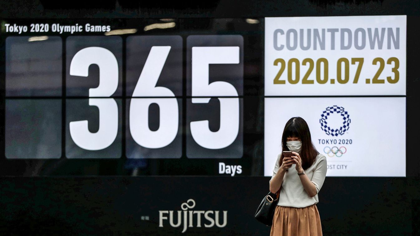 A woman wearing a protective face mask stands in front of a screen showing a countdown of the days to the Tokyo 2020 Olympic Games amid the coronavirus disease (COVID-19) outbreak, in Tokyo