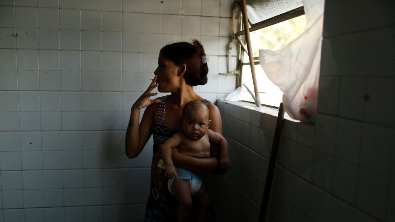 A woman holding her baby smokes a cigarette as she waits for a washing machine, before doing laundry inside the bathroom at the Nova Tuffy slum, in an abandoned factory in Rio de Janeiro
