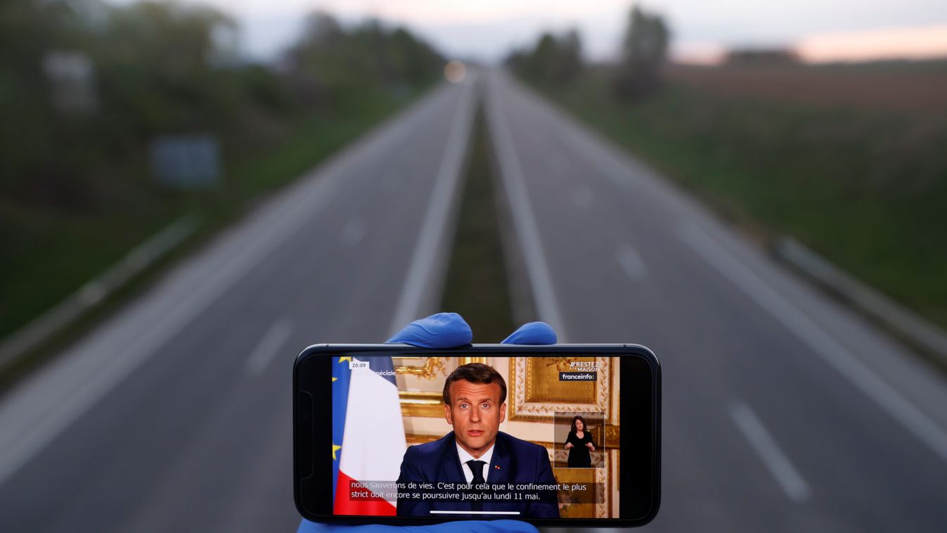A mobile phone showing French President Emmanuel Macron, as he addresses the nation about the coronavirus disease (COVID-19) outbreak is displayed for a phot in front of an almost empty motorway in Strasbourg