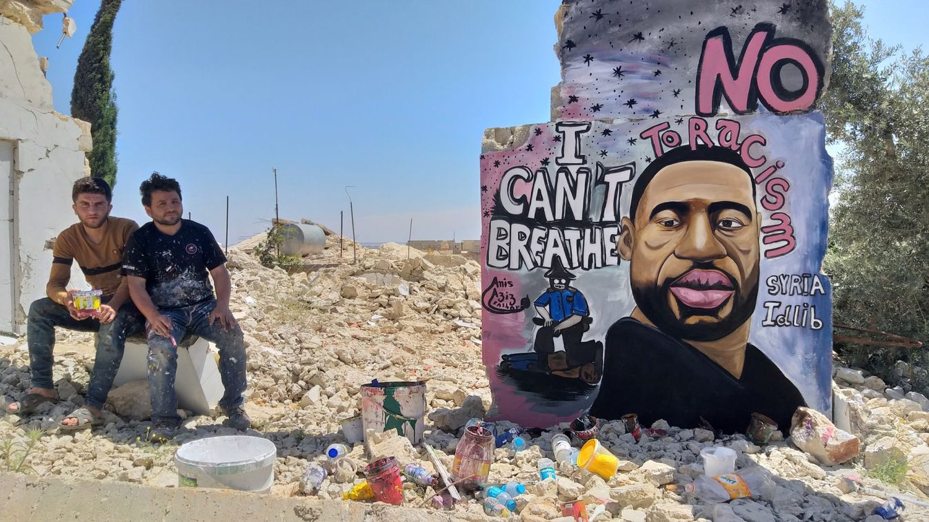 Artists Aziz Asmr and Anis Hamdoun pose next to a graffiti of George Floyd in Idlib