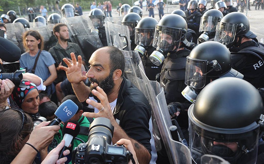 A migrant talks to the media in front of Hungarian riot police at the border crossing with Serbia in Roszke