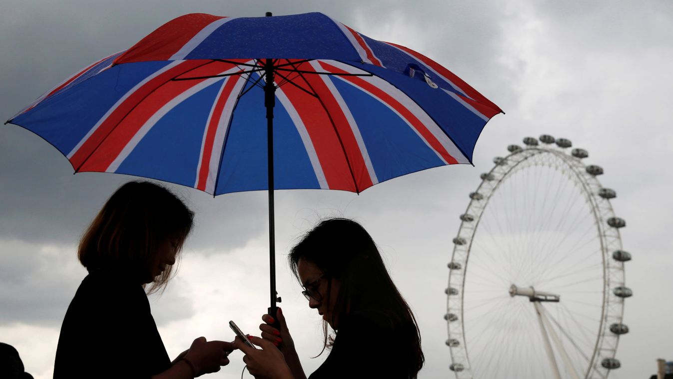 Women look at their phones under a Union Flag umbrella, after official celebrations for Britain Queen Elizabeth's 90th birthday, near the London Eye in London