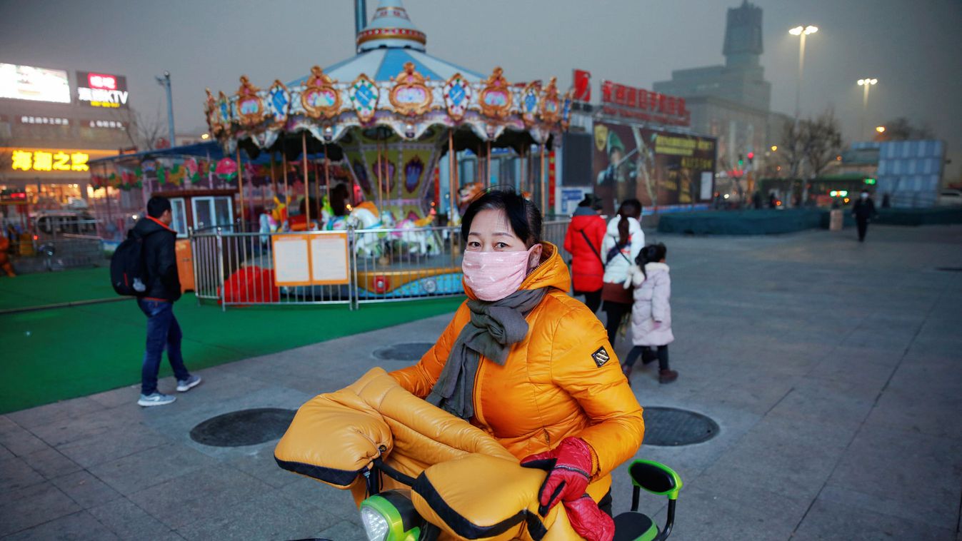A woman wearing a face mask rides a moped on an extremely polluted day with red alert issued, in Langfang