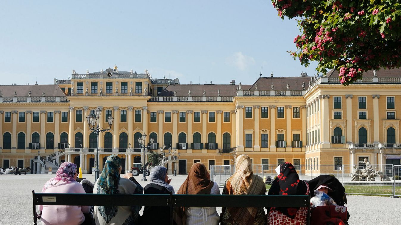 Women and children enjoy the morning sun on a bench in front of Schoenbrunn castle in Vienna