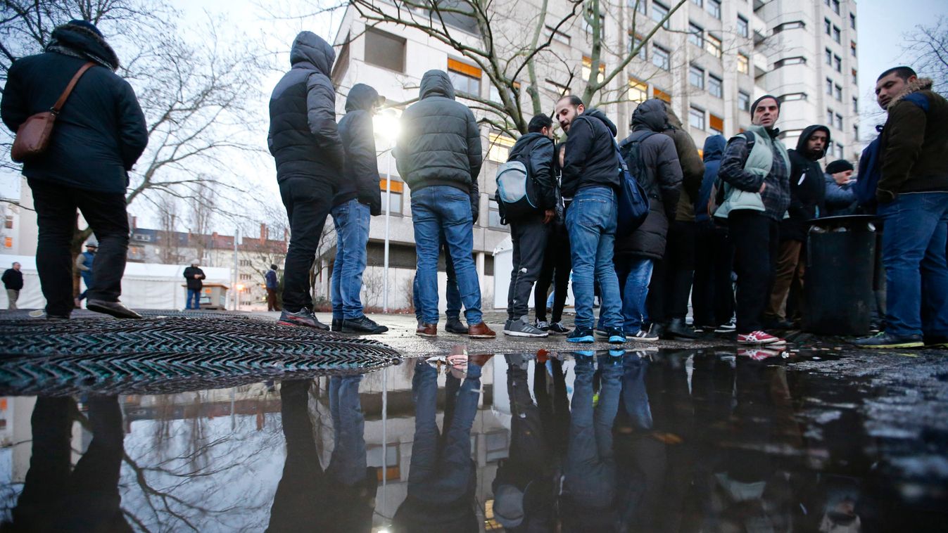Migrants are reflected in a puddle as they queue in front of the compound of the Berlin Office of Health and Social Affairs in Berlin