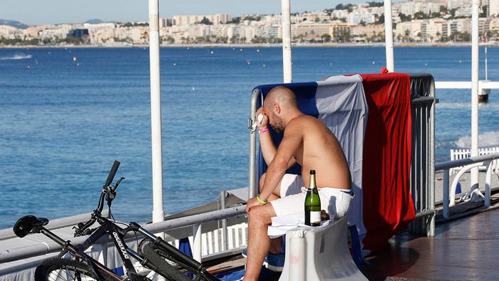 A man reacts as he sits near a French flag along the beachfront the day after a truck ran into a crowd at high speed killing scores celebrating the Bastille Day July 14 national holiday on the Promenade des Anglais in Nice