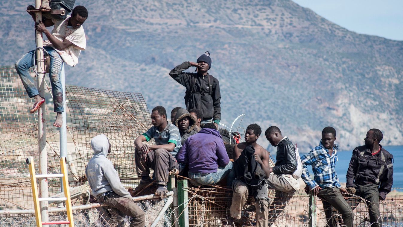 African migrants sit on top of a border fence between Morocco and Melilla