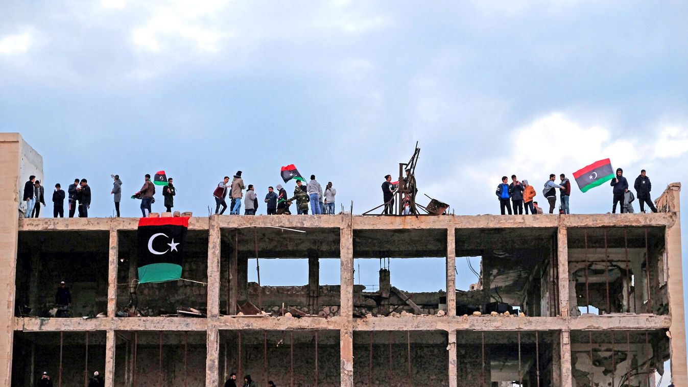 Men hold Libyan flags atop the court building during a celebration of the eighth anniversary of the revolution, in Benghazi