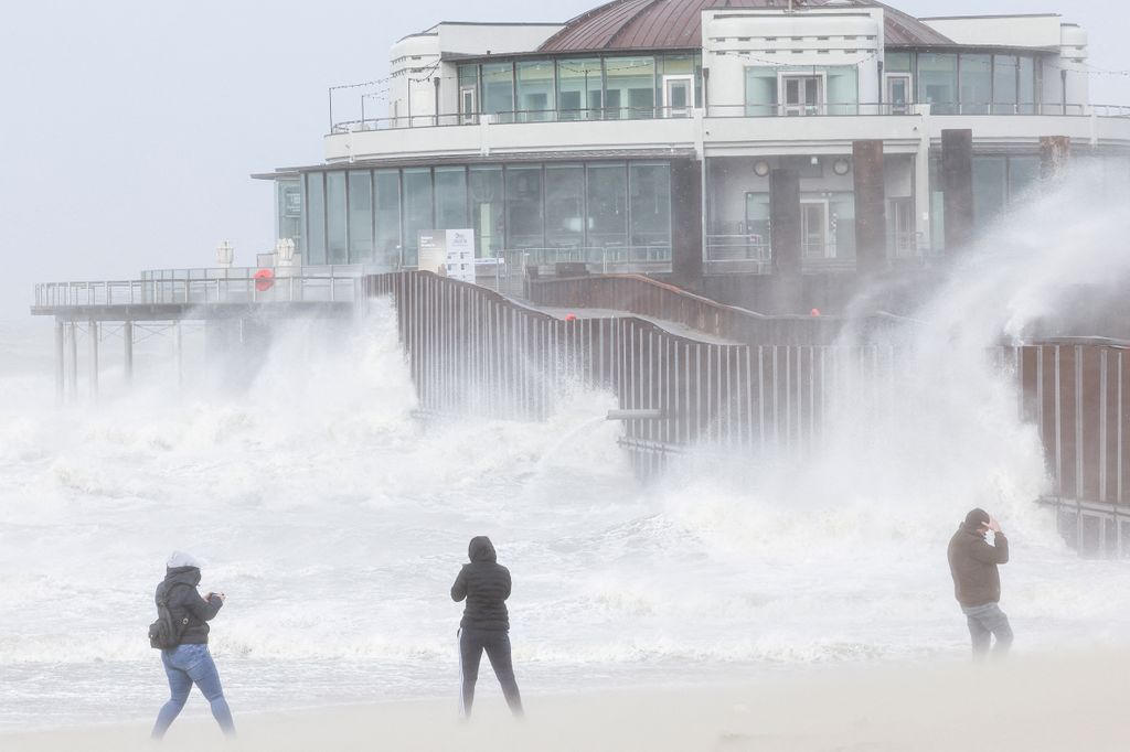 People walk as waves break on the beach in the wake of Storm Eunice in Blankenberge, Belgium, February 18, 2022. REUTERS/Yves Herman  REFILE - CORRECTING CITY