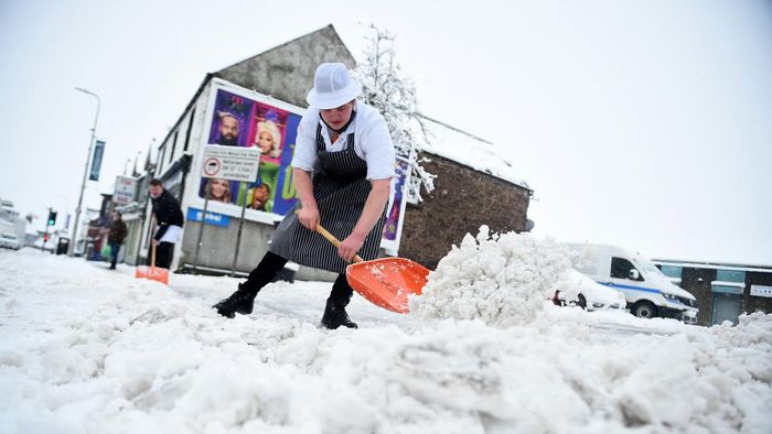 Butchers shovel the snow from the path outside their shop in Auchterarder, central Scotland, on February 18, 2022, as Storm Eunice brings high winds across the country. - Britain put the army on standby Friday and schools closed as forecasters issued two rare "red weather" warnings of "danger to life" from fearsome winds and flooding due to the approaching storm Eunice. (Photo by ANDY BUCHANAN / AFP)